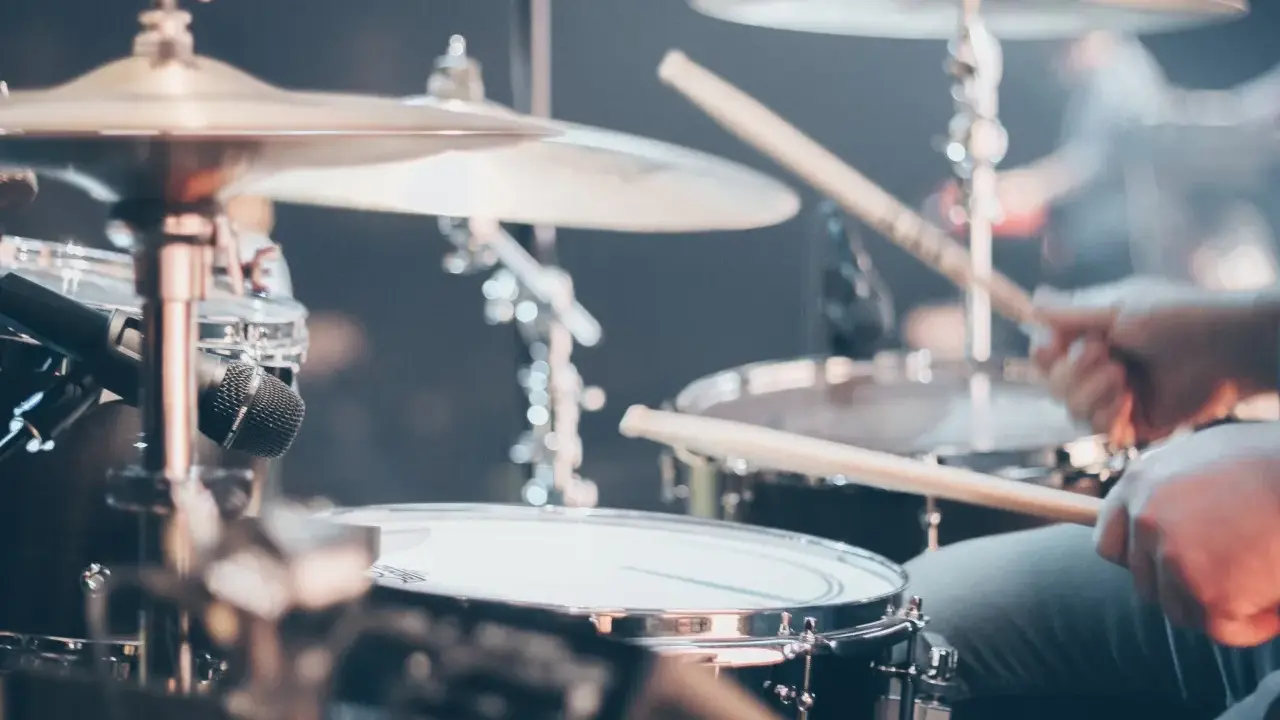 Gros plan sur un set de batterie, avec des baguettes en action. Différents types de tambour et cymbales sont visibles.