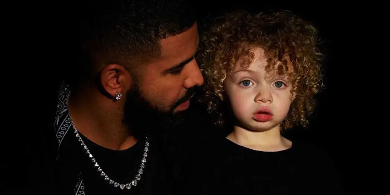 Drake i jego syn, Adonis, w czarnych ubraniach. Chłopiec ma kręcone, jasne włosy i niebieskie oczy.