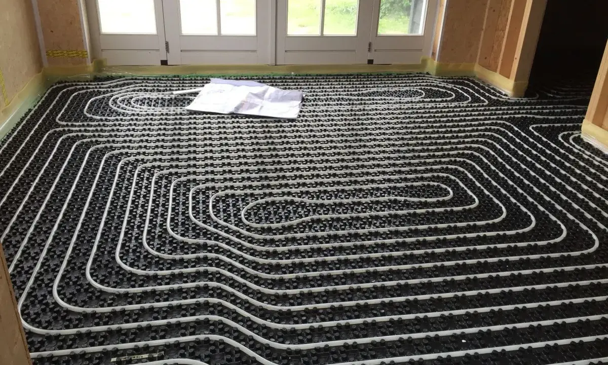 Instalación suelo radiante con tuberías blancas sobre paneles negros. Un plano yace sobre el suelo.