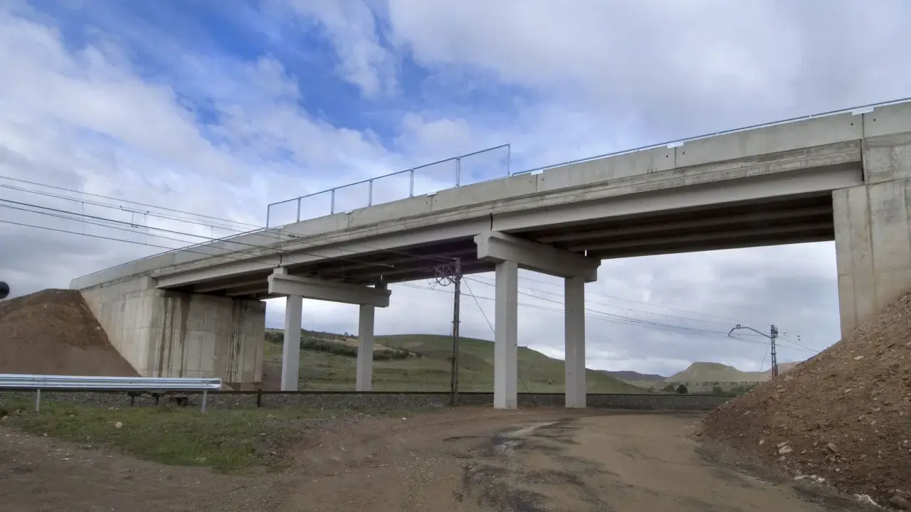 Un puente de hormigón cruza vías de tren. Los pilares de soporte, que son un estribo, sostienen la estructura. El cielo está nublado.