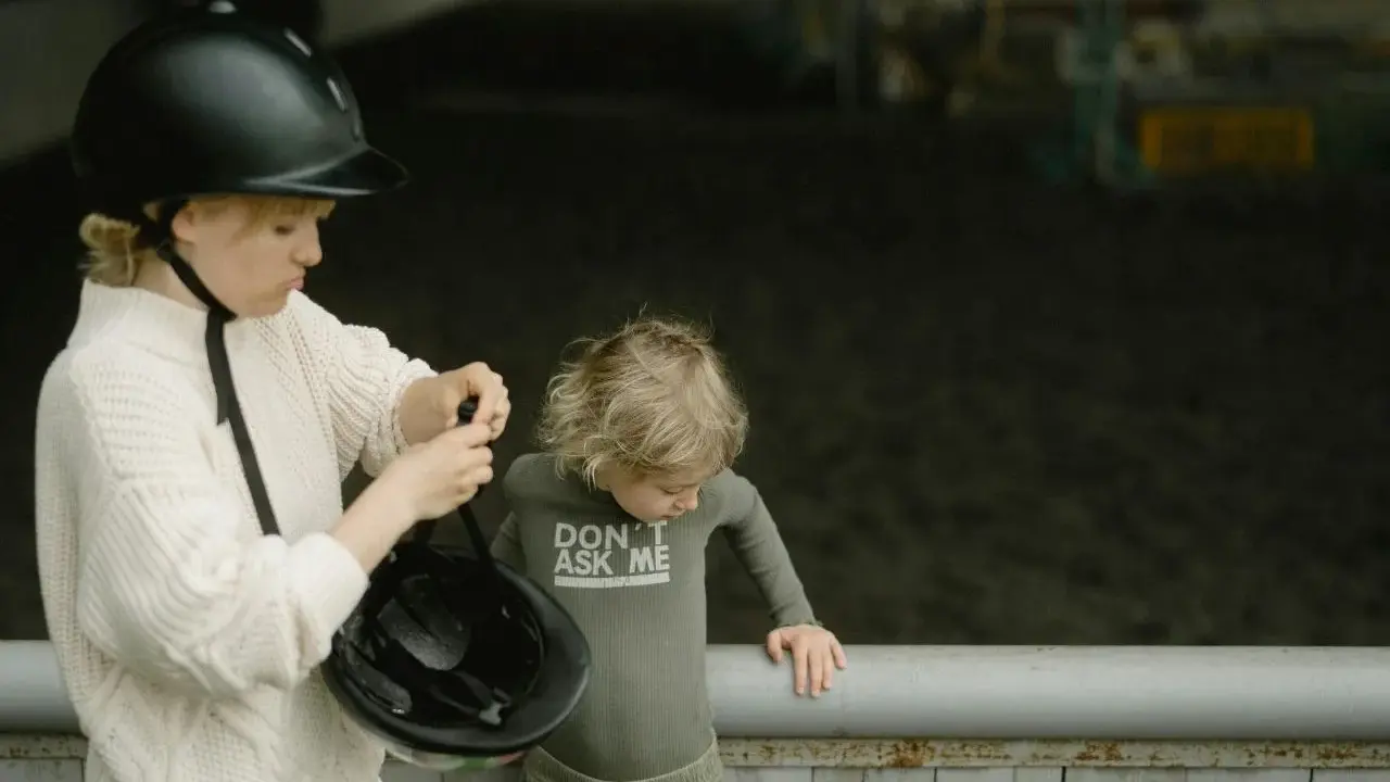Starsza dziewczynka w kasku pokazuje młodszemu dziecku, jak zmierzyć głowę na kask, przygotowując się do jazdy konnej.