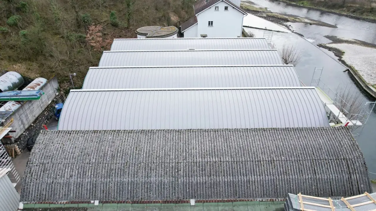 Reihen von Sheddach-Konstruktionen mit Metall- und Wellplatten. Ein Fluss und ein Gebäude sind im Hintergrund zu sehen.