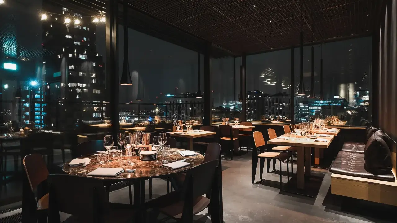 En mysig restaurang i Stockholm med vacker utsikt över stadens ljus på natten. Eleganta bord med dukning och bekväma sittplatser.