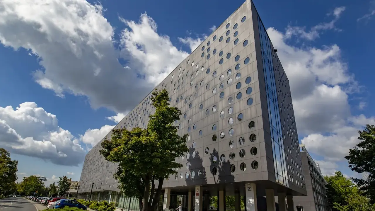 Nowoczesny budynek SWPS Wrocław z okrągłymi oknami, pod błękitnym niebem z chmurami.