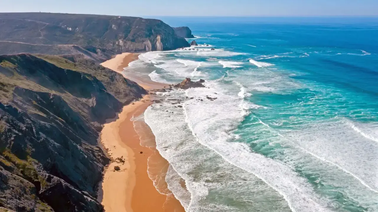 Atemberaubende Küstenlandschaft im Distrikt Faro, Portugal. Steile Klippen treffen auf einen goldenen Sandstrand und das türkisfarbene Meer mit tosenden Wellen.