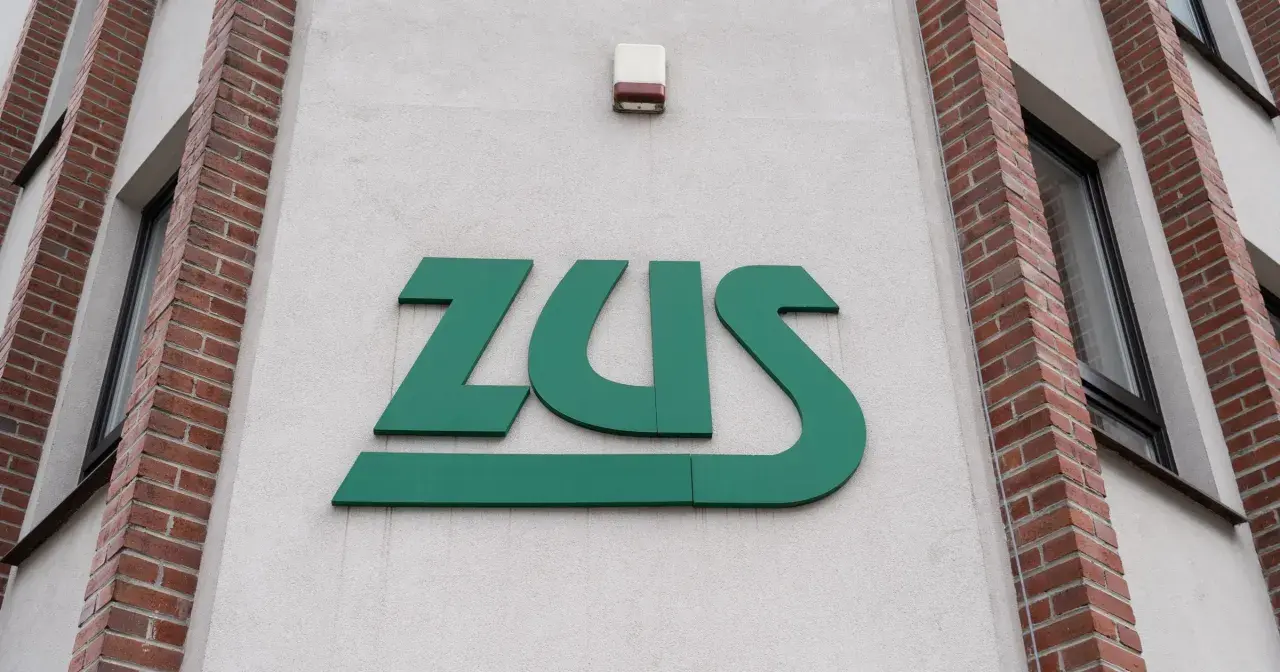 Zielone logo ZUS na białej ścianie budynku z ceglanymi elementami.