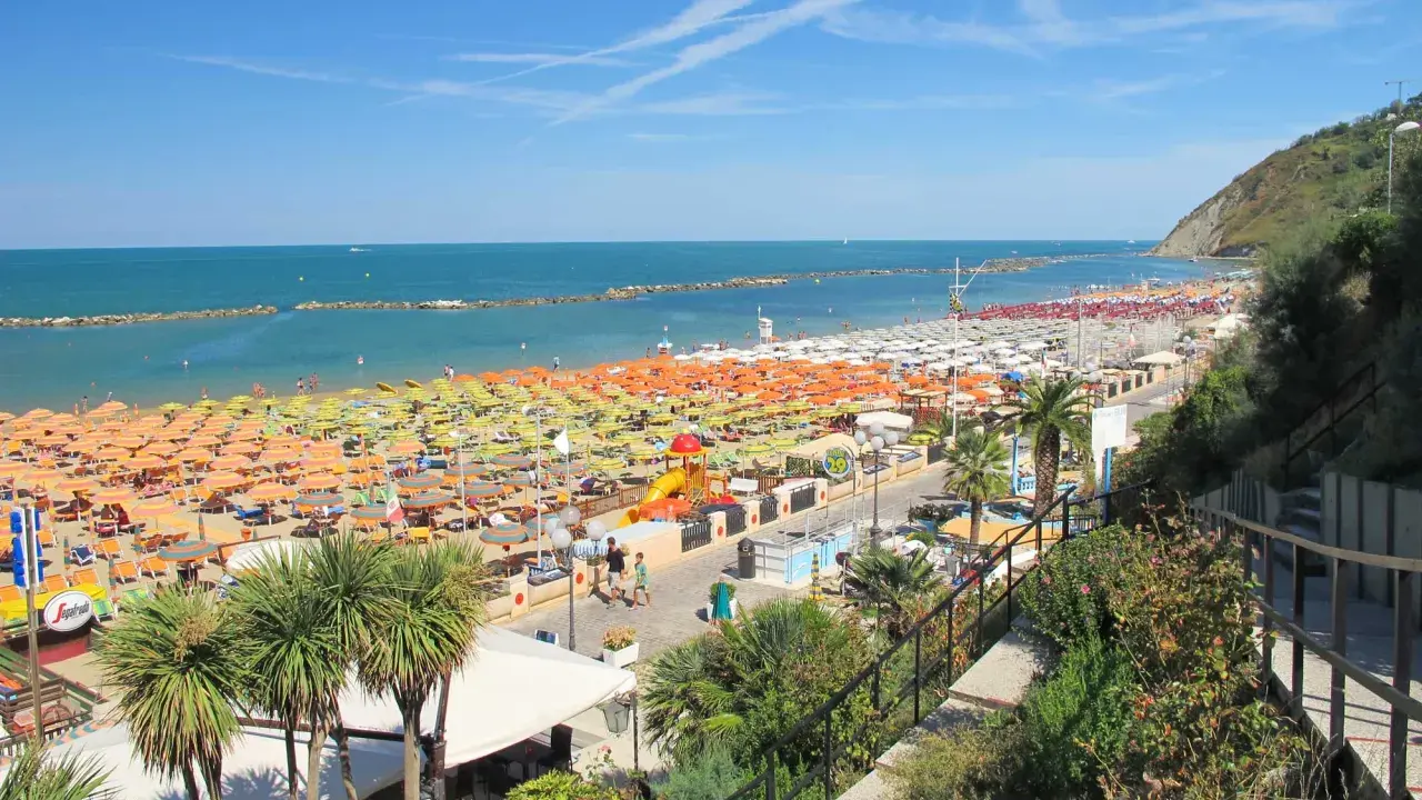 Ampia spiaggia libera a Gabicce Mare, con file infinite di ombrelloni colorati e lettini sotto un cielo azzurro.