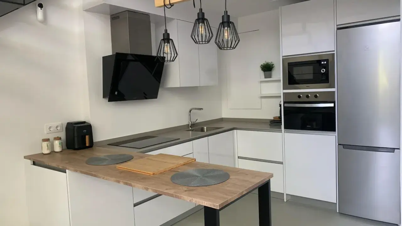 Cocina moderna con isla, electrodomésticos integrados y lámparas colgantes. Ideas para como diseñar una cocina funcional y elegante.