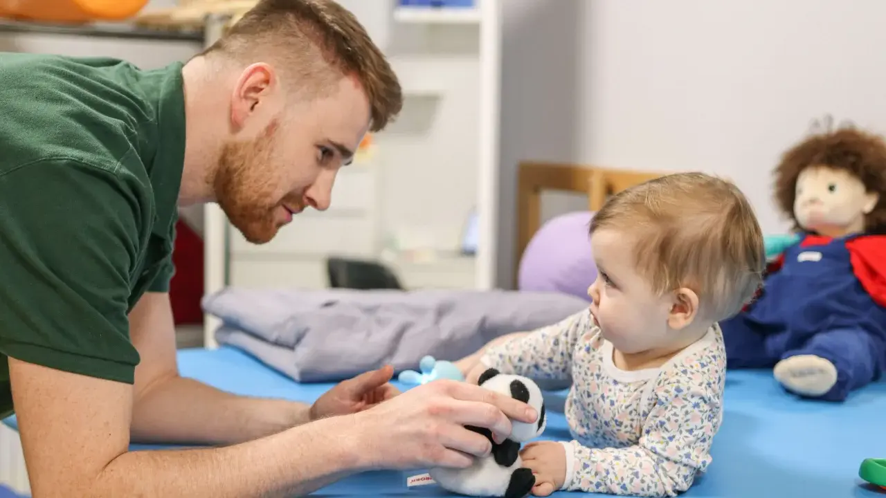 Osteopata dla dzieci delikatnie bawi się z niemowlęciem pluszową pandą, wspierając jego rozwój.