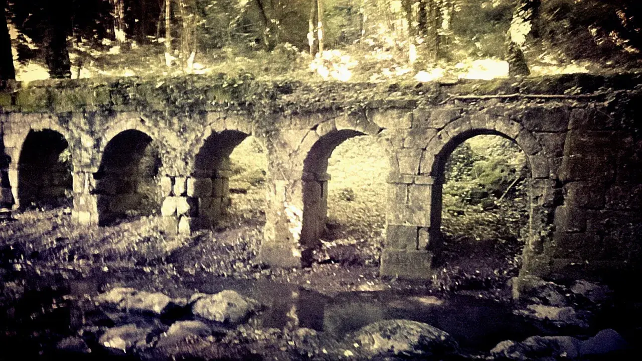 Antica struttura in pietra con archi, forse un acquedotto o un ponte, immersa nel verde. La **vitozza Sorano** sembra un luogo dimenticato dal tempo.