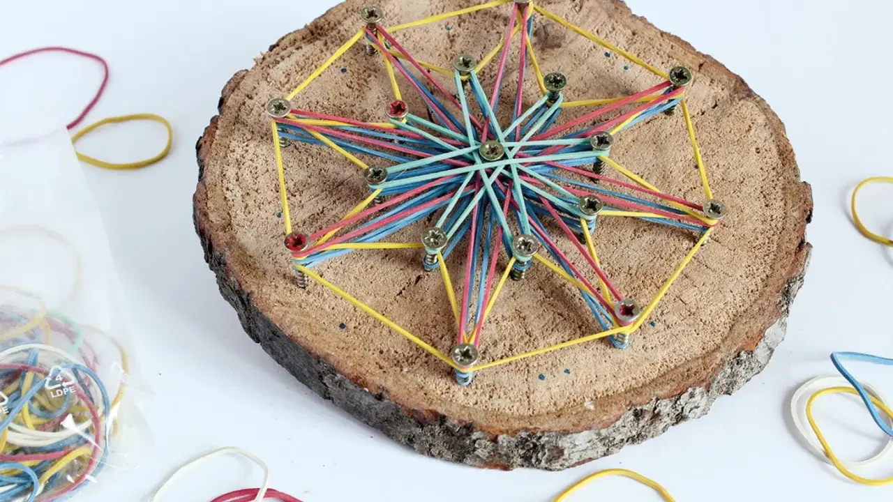 Bunte Gummibänder spannen sich zu einem Stern auf einer Baumscheibe. Ein tolles Bastelprojekt für Kinder, das Kreativität und Feinmotorik fördert.