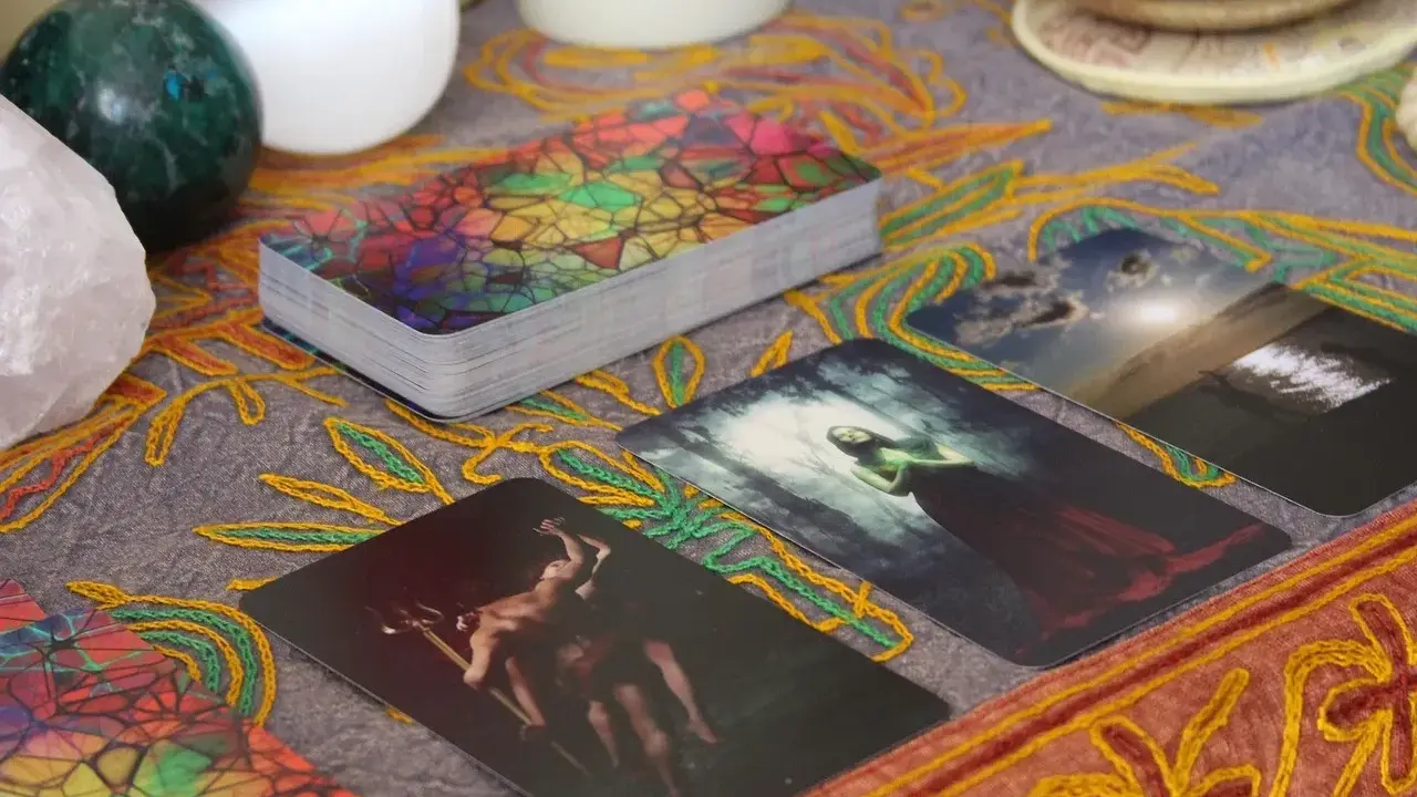 Tarot dzienny ryby: karty z mistycznymi obrazami, kryształ, kule i ozdobny obrus tworzą atmosferę wróżenia.