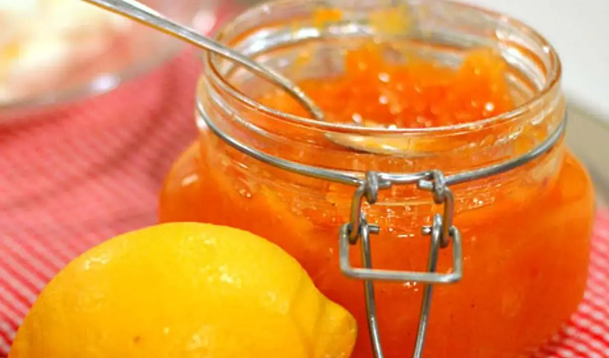 En burk med hemgjord citronmarmelad och en färsk citron på en rödvitrutig duk.