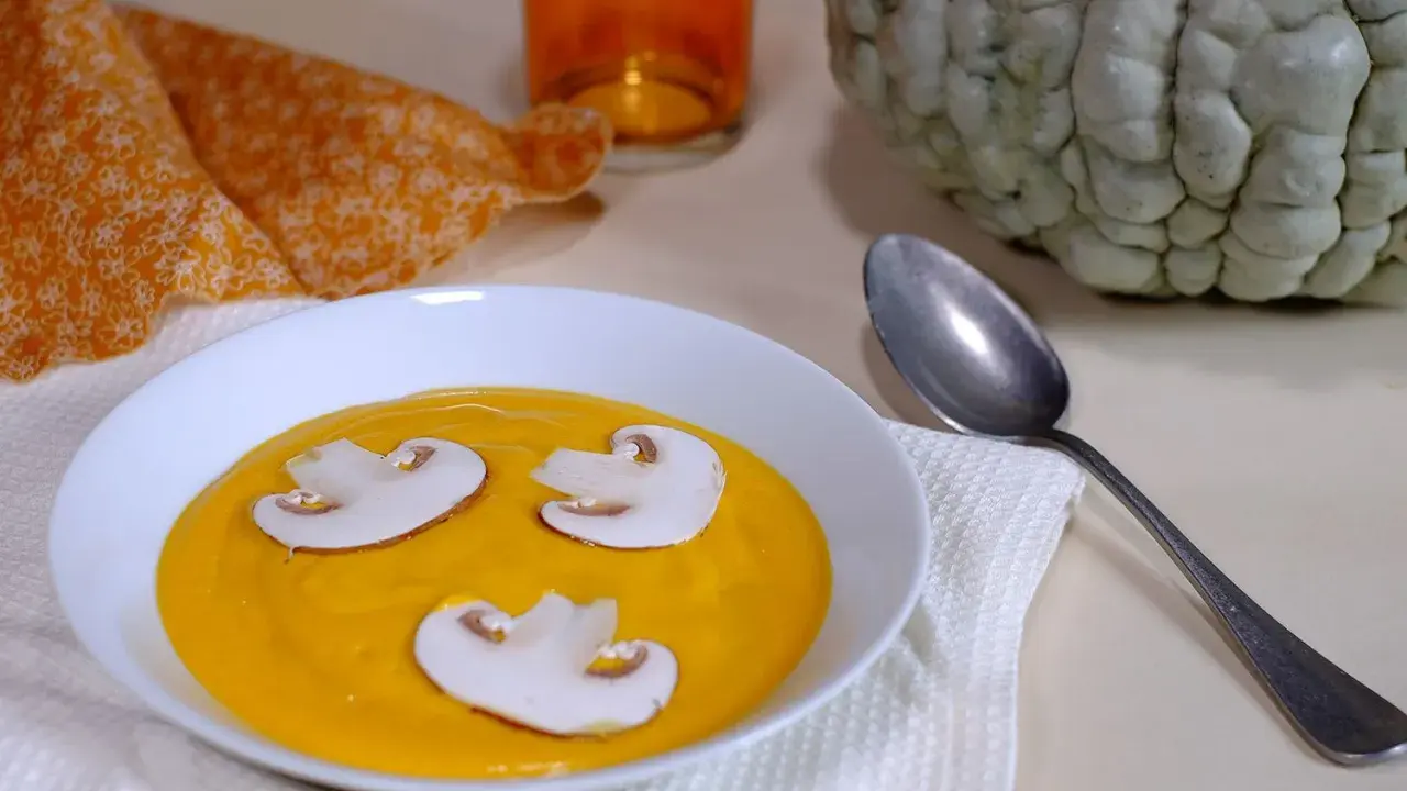 Soupe de courge orange avec des champignons, une serviette orange et une courge entière, évoquant une ambiance de Marina di Chioggia.