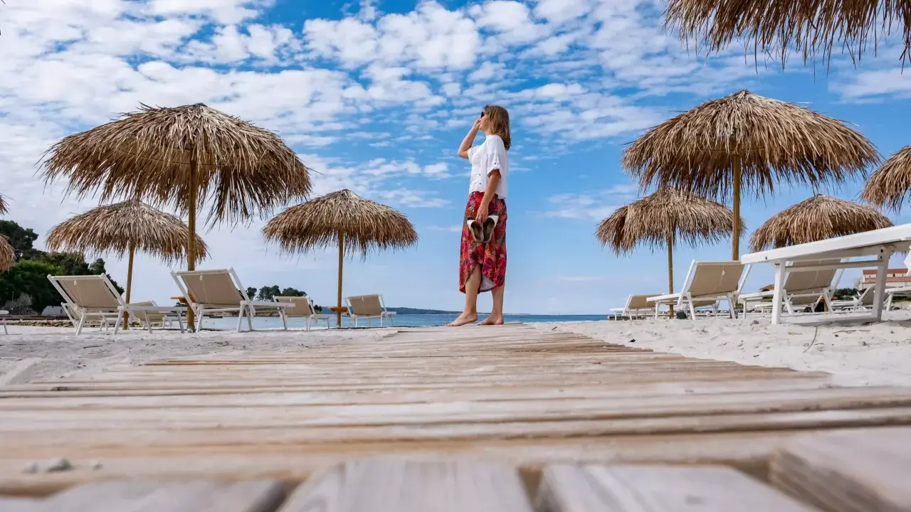 Kobieta na plaży, pod słomianymi parasolami, podziwia widok. To idealne miejsce na wyspie Rab, atrakcje czekają!
