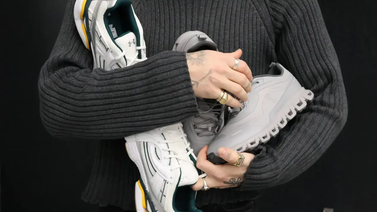 Person hält drei Paar Sneaker: weiße mit grünen Akzenten, graue und silberne. Ein Blick auf modernes shoe design.