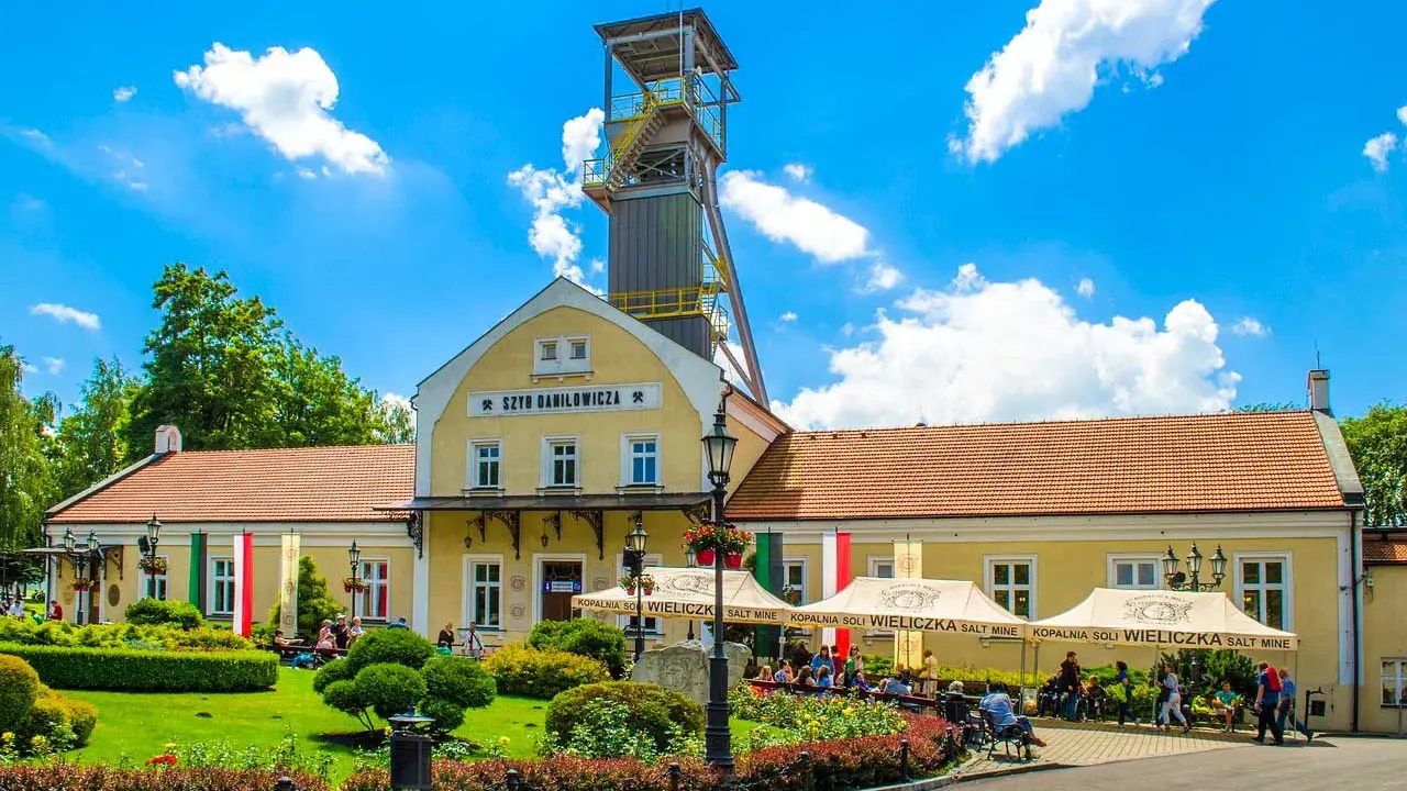 Wieliczka atrakcje: Szyb Daniłowicza, żółte budynki kopalni, zielony ogród i ludzie odpoczywający pod namiotami.