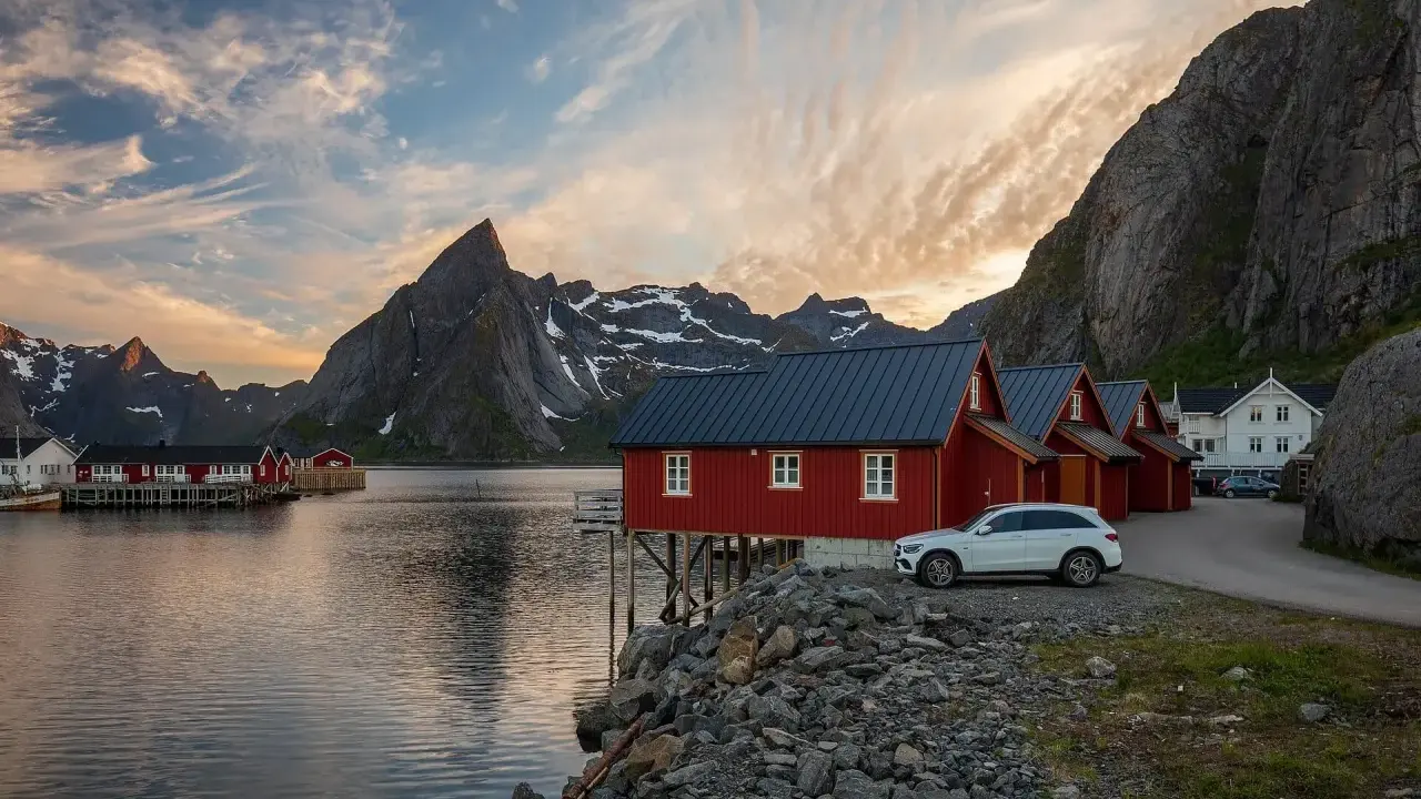 Röda fiskestugor vid vattnet i Lofoten, perfekt boende för en stuga-semester med dramatiska berg i bakgrunden.