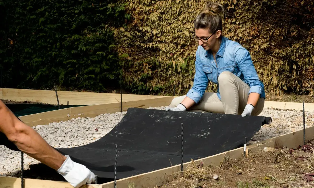 Preparando el terreno para saber como hacer hormigón para suelo. Colocando tela geotextil dentro de encofrado de madera.