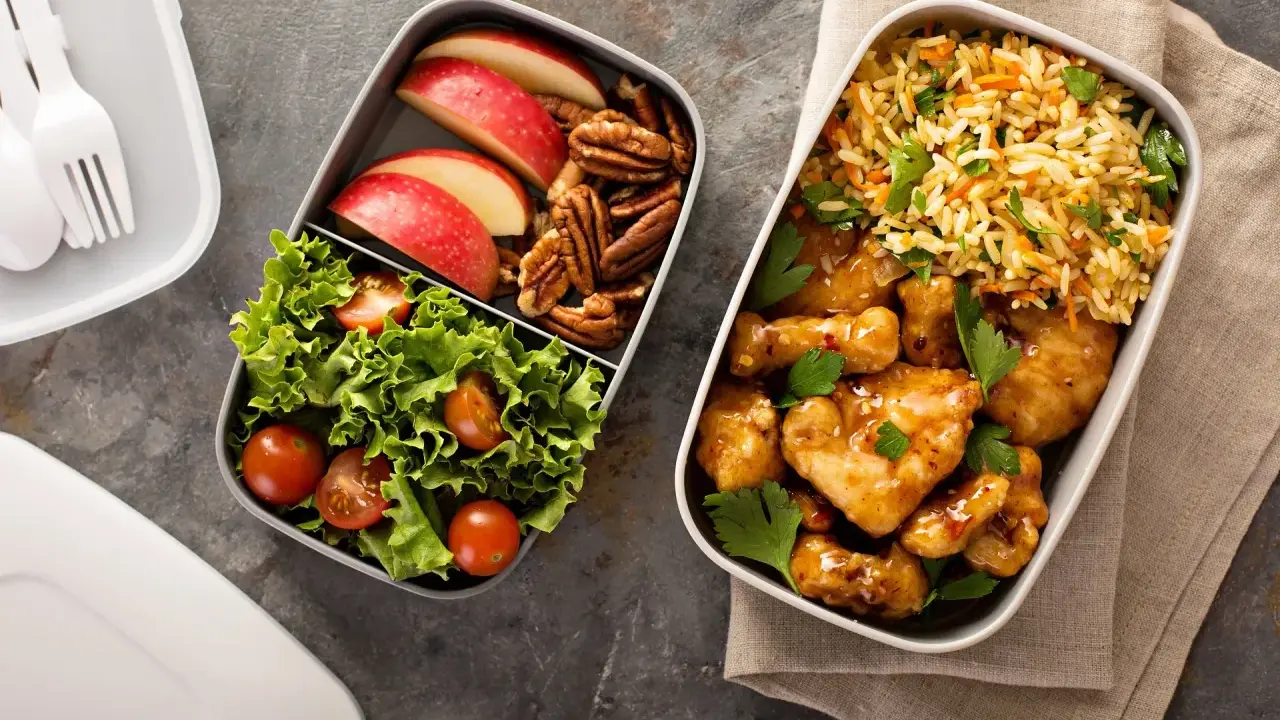 Dwa pojemniki z jedzeniem: jeden z kurczakiem w sosie, ryżem i natką, drugi z sałatką, jabłkami i orzechami. Idealne fit przepisy airfryer na lunch.