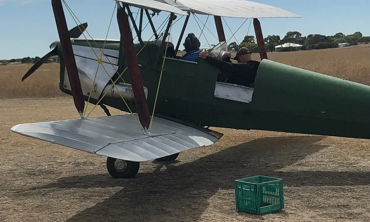 Grüner Doppeldecker, bereit zum Start. Ein Pilot und ein Passagier sitzen im Cockpit. Das Flugzeug erinnert an einen Tiger Moth.