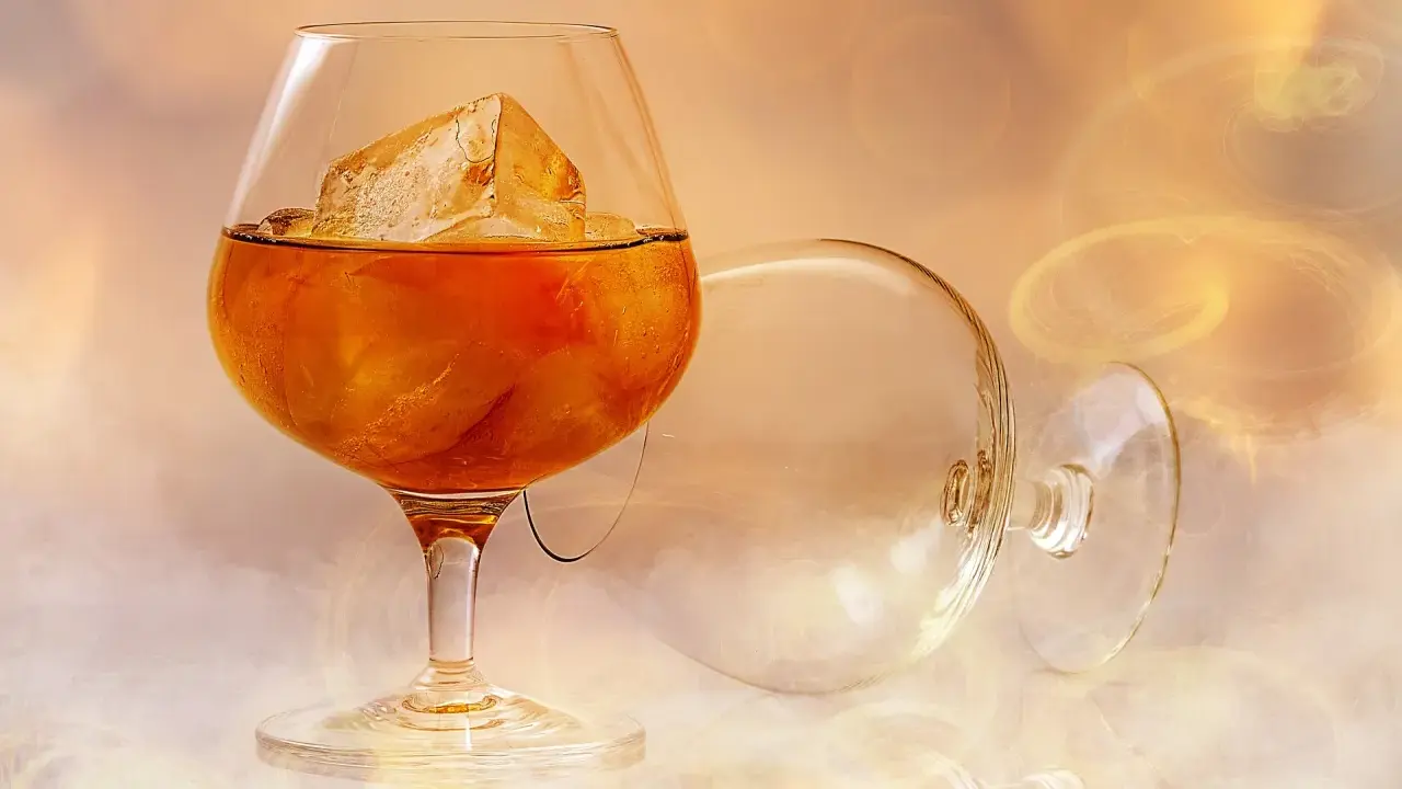 Ein Glas mit bernsteinfarbenem Brandy und Eiswürfeln steht neben einem leeren, umgekippten Glas. Was ist ein Brandy? Ein edles Getränk.