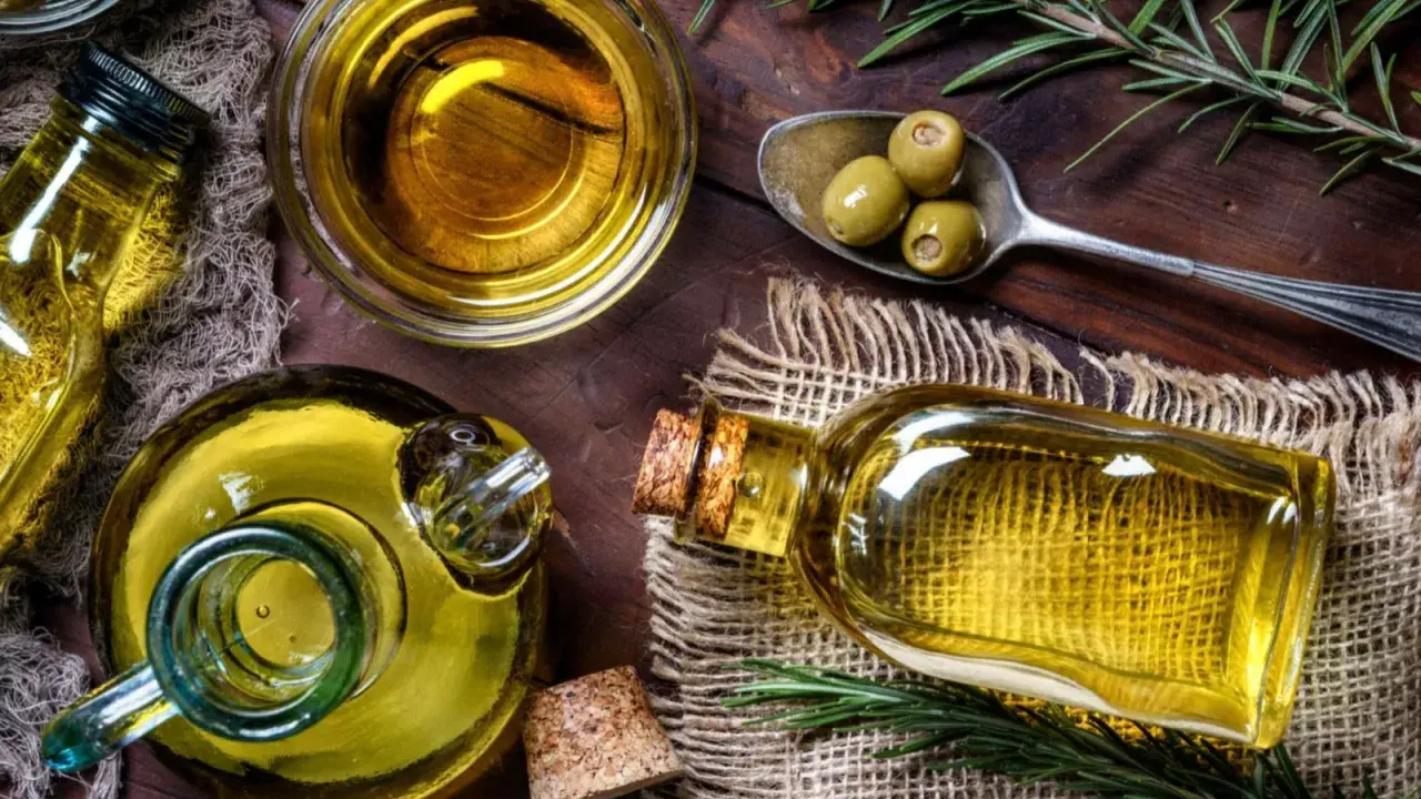 Aceite de oliva en botellas y cuenco, con aceitunas y romero. A pesar de sus beneficios, hay desventajas del aceite de oliva, como su precio.