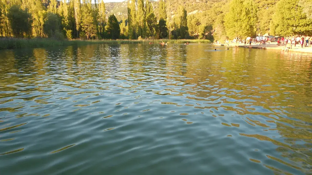Gente disfrutando del agua en la playa de Cañamares, rodeada de árboles y montañas.