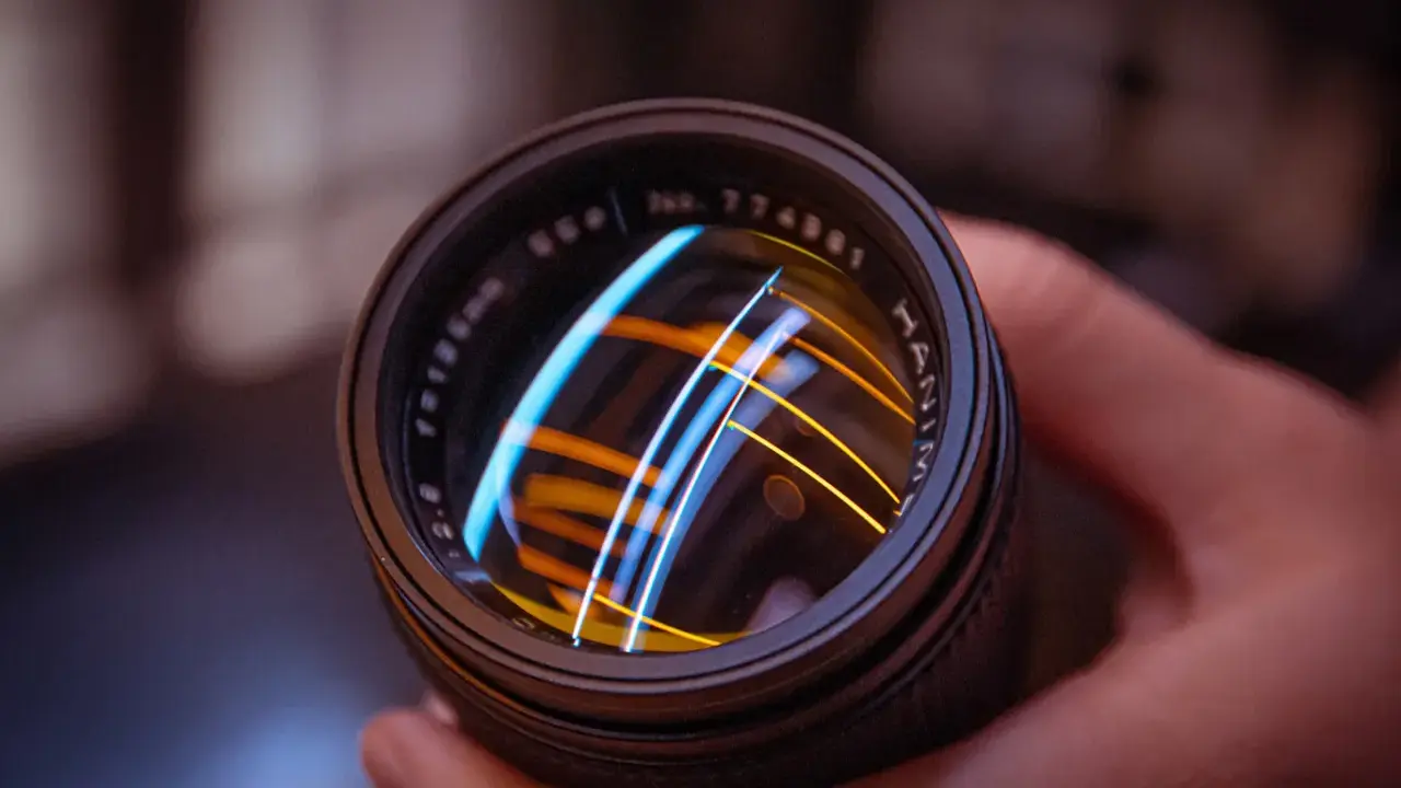 Primer plano de un objetivo fotográfico con reflejos de luces azules y naranjas.