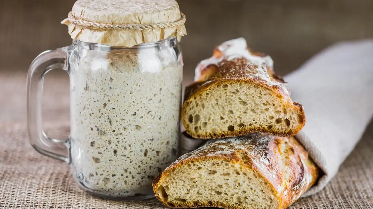 Un bocal de levain actif, prêt à être utilisé pour entretenir son levain, à côté de deux belles tranches de pain artisanal.
