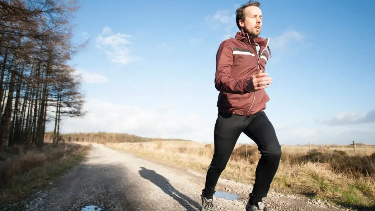 Mann joggt bei 10 Grad in einer leichten Jacke und Hose auf einem Feldweg.