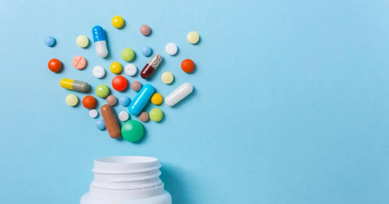 Różnorodne tabletki i kapsułki wysypujące się z białego pojemnika. Czy to opioidy, co to za leki?