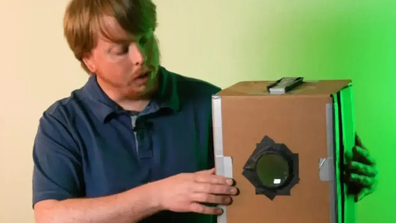 Mężczyzna prezentuje domową camera obscura z kartonu.