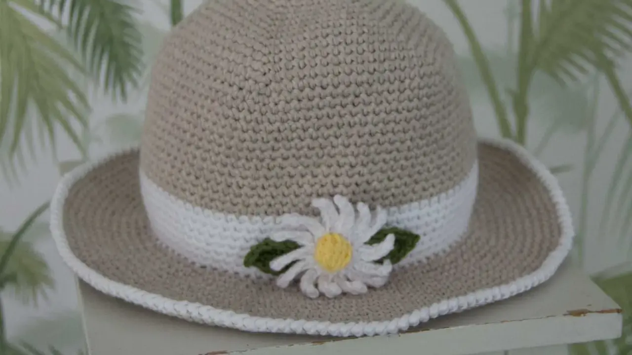 En virkad solhatt för barn, beige med vit kant och en söt blomdekor. Perfekt för soliga dagar!