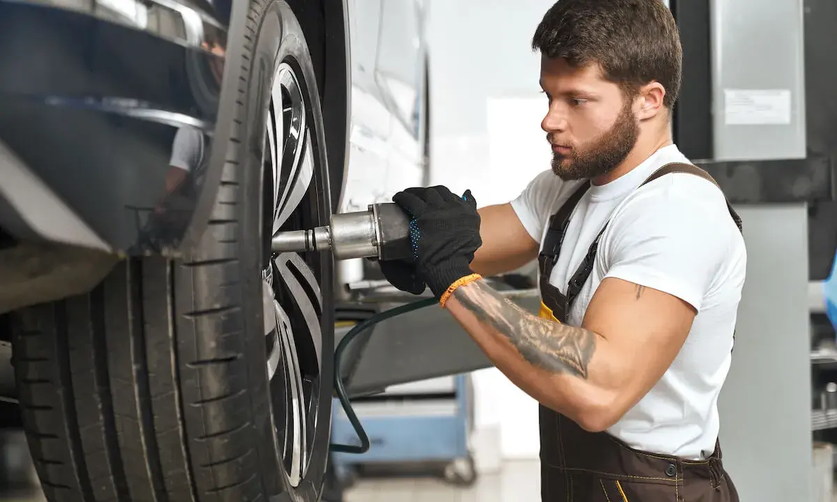 Mechanik z tatuażem dokręca śrubę koła. Zwróć uwagę na objawy zużycia sworznia wahacza, gdy słyszysz stuki.
