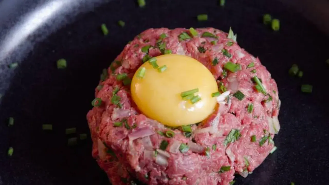 Delicioso steak tartar de wagyu con yema de huevo y cebollino picado, servido en un plato negro.