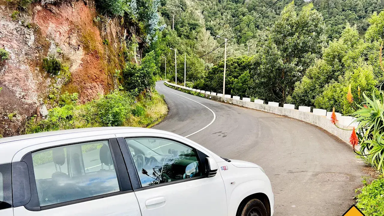 Weißes Auto auf einer kurvigen Straße auf Madeira. Die Fahrt durch die üppige grüne Landschaft ist ein Abenteuer.