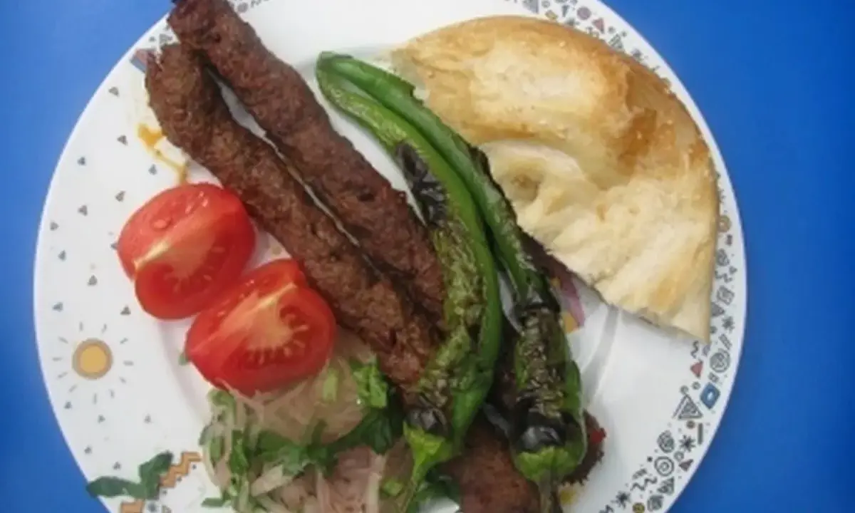 Adana Kebap mit gegrillten Peperoni, Tomaten und Fladenbrot auf einem Teller.