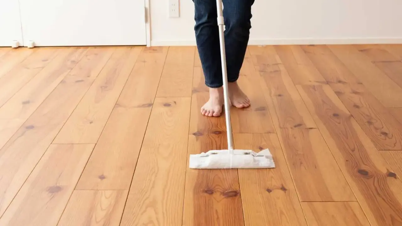 Persona descalza limpiando parquet con una mopa. El suelo de madera luce brillante y cuidado.