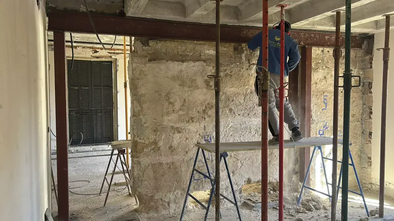 Trabajador realiza el empresillado de pilares en una obra. Se aprecian puntales metálicos y vigas de soporte.
