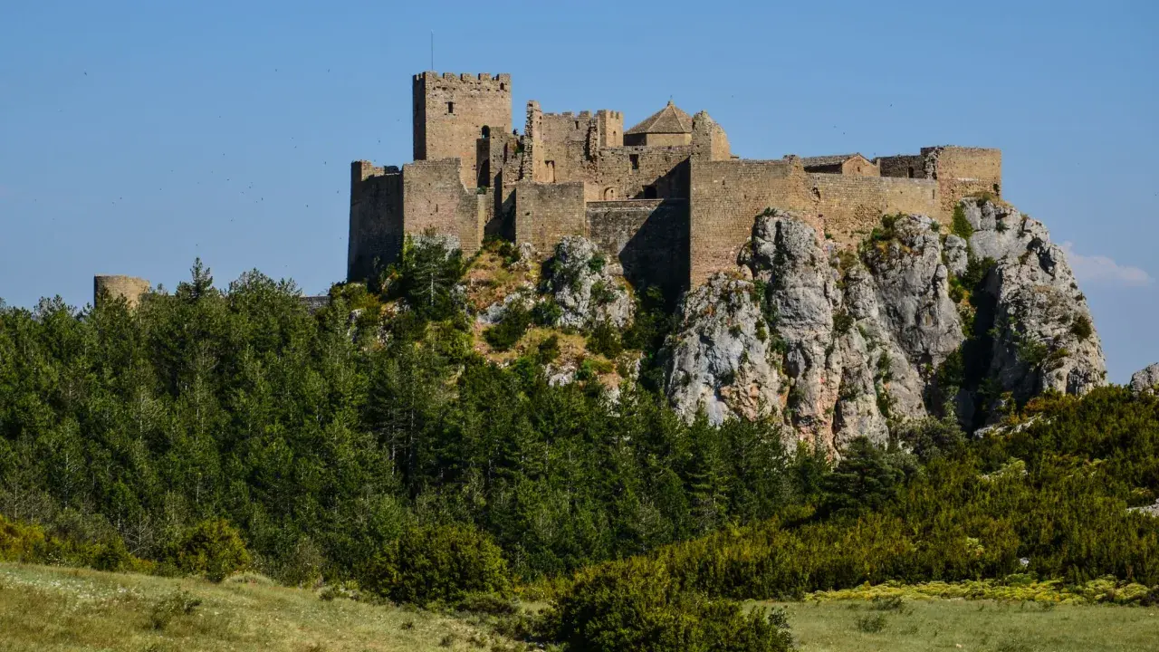 Das Castillo de Loarre thront majestätisch auf einem Felsen, umgeben von grünen Wäldern und unter blauem Himmel.