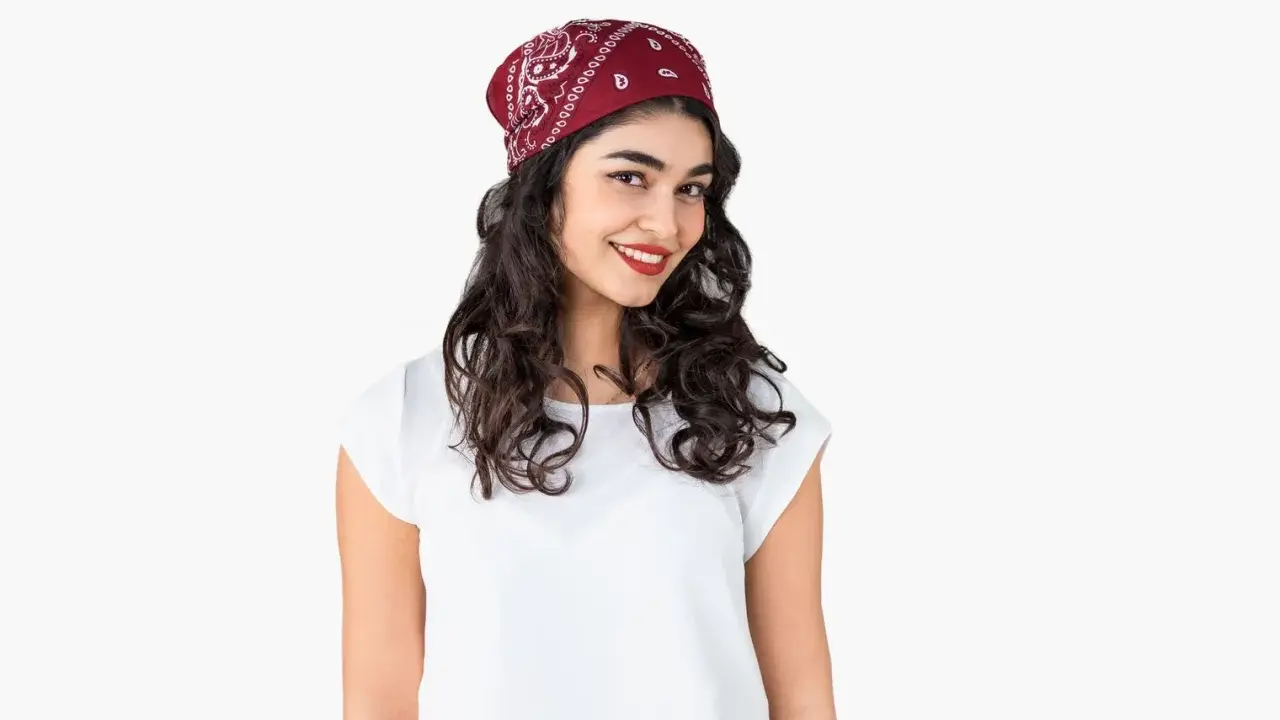 Uśmiechnięta dziewczyna z burzą loków, na głowie ma czerwoną bandana. Pokazujemy, jak zawiązać chustę na głowie.