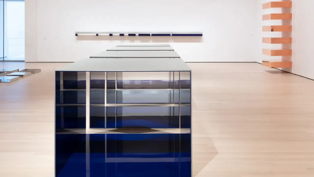 Installazione di Donald Judd con elementi blu e metallici su pavimento in legno chiaro, in una galleria d'arte.