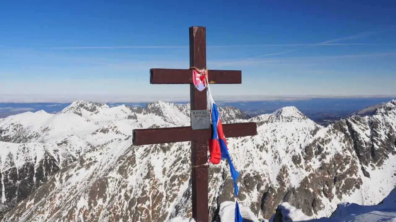 Drewniany krzyż z flagą Słowacji na szczycie Kriváň, narodowej góry Słowaków, na tle ośnieżonych Tatr.
