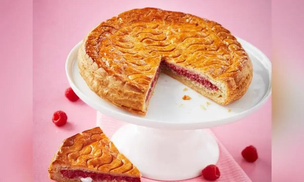 Galette framboise dorée sur un présentoir blanc, une part coupée révèle la garniture rose. Parfait pour une recette galette framboise.