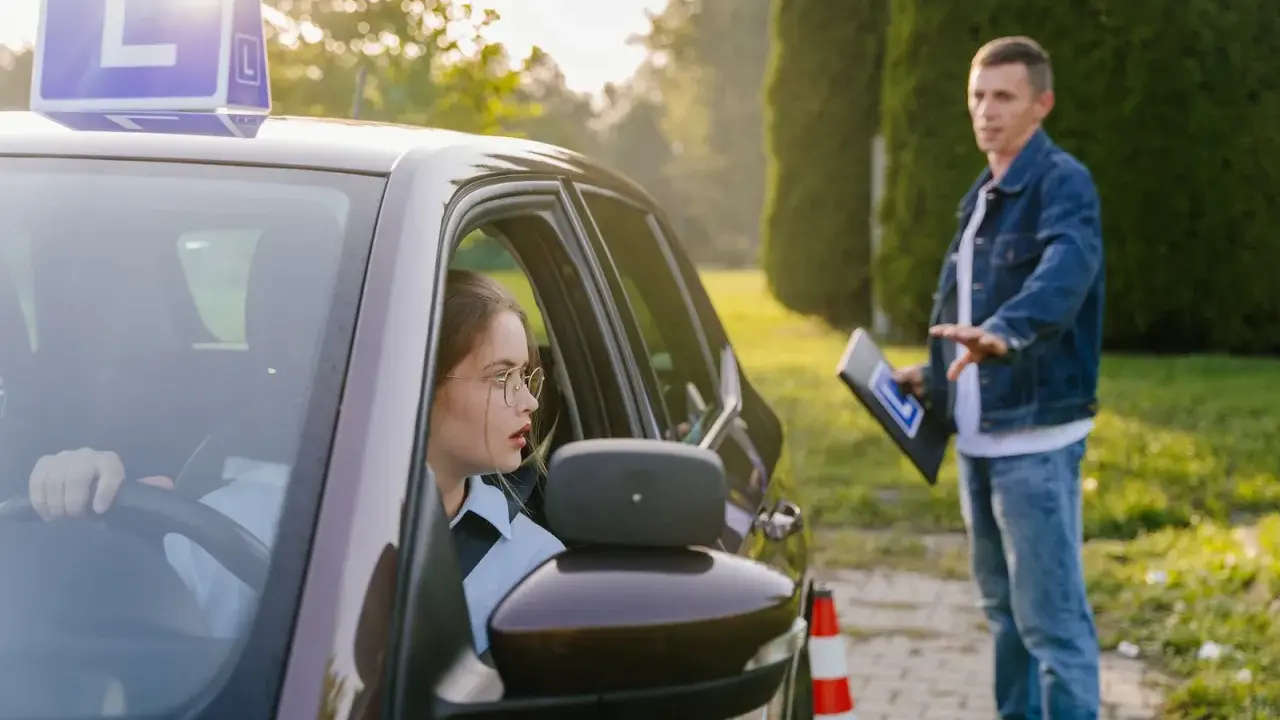 Młoda kobieta w okularach uczy się jeździć, a instruktor pokazuje jej, ile ważny jest kurs prawa jazdy.