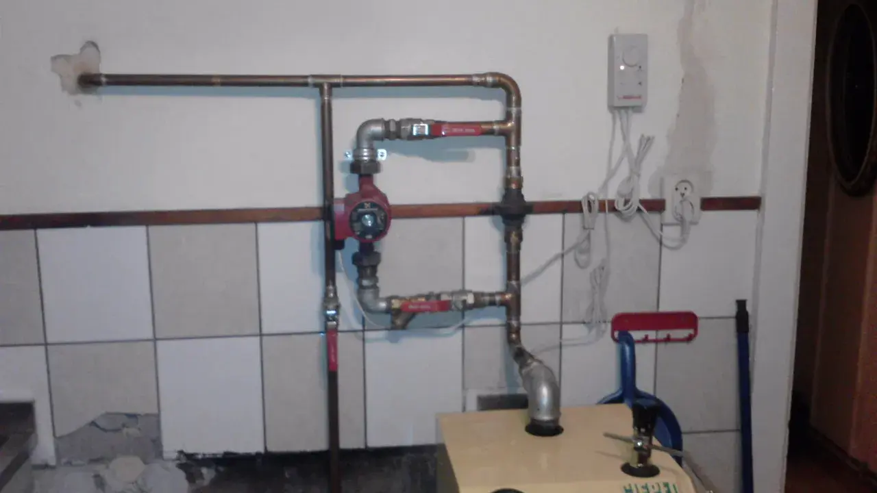 Montaż pompy CO w układzie otwartym. Widoczna instalacja hydrauliczna, czerwona pompa, zawory i fragment kotła.