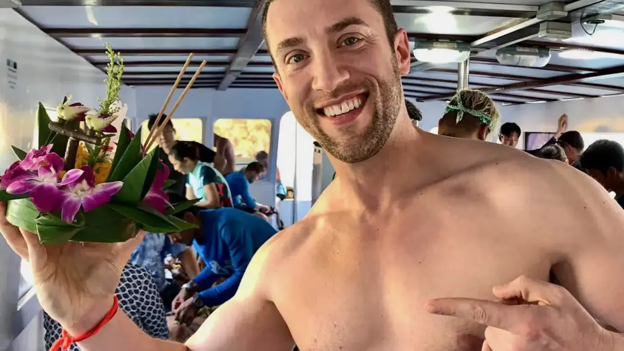 Smiling man on a boat in Asia, holding a flower offering. A perfect moment for gay travel in Asia.