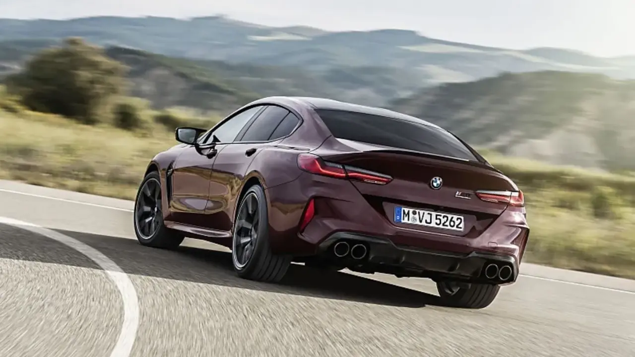 Ein dunkelroter BMW M8 Gran Coupé rast auf einer kurvigen Straße durch eine hügelige Landschaft.