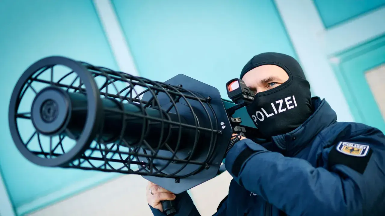 Polizist mit Sturmhaube und "POLIZEI"-Aufdruck zielt mit einer Drohnenabwehrwaffe.
